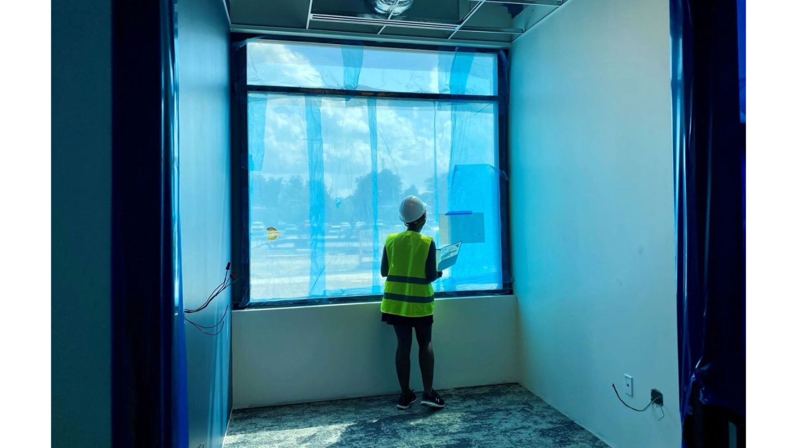 Entrepreneur in hard hat and safety vest looking out window of newly constructed office at Ascend704.